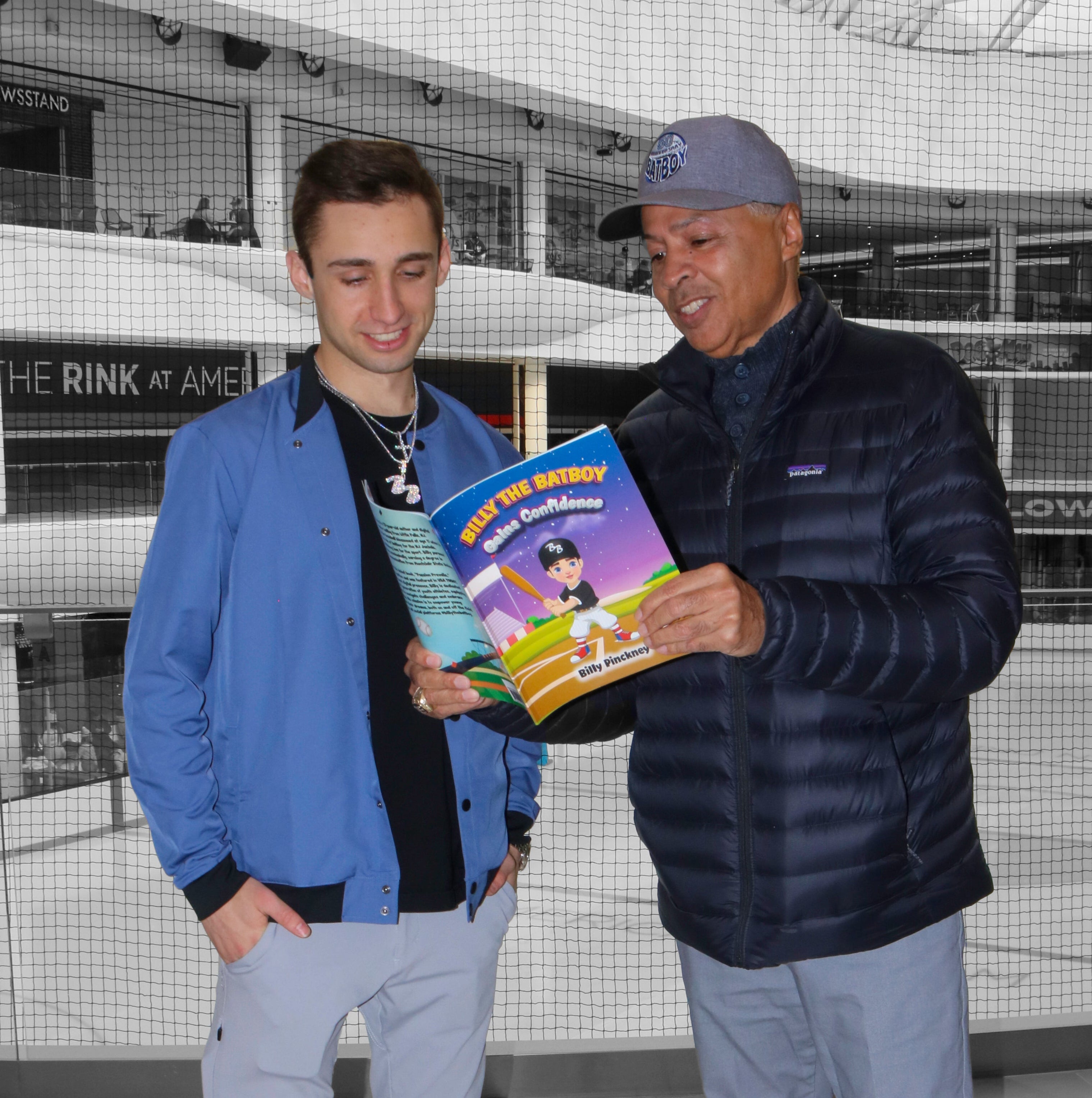 Two men standing in a modern indoor mall, one holding a book.